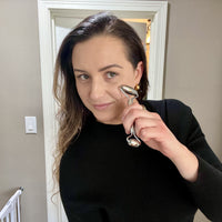 Woman using stainless steel facial roller for skincare routine at home