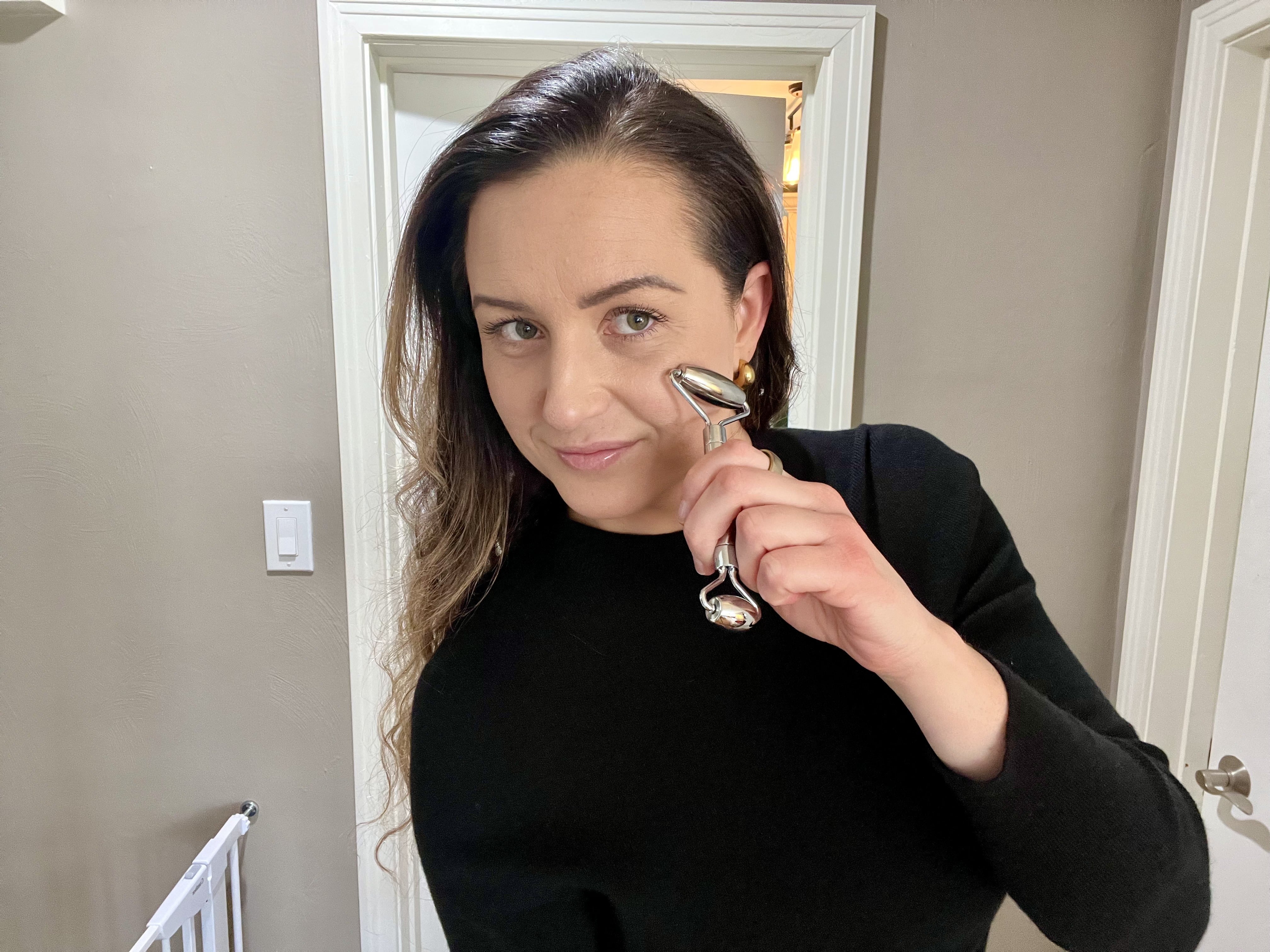 Woman using stainless steel facial roller for skincare routine at home